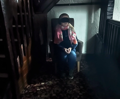Kindred Spirit Investigations ghost hunt visitor with headphones and blindfold sat on chair next to stairs in haunted pub