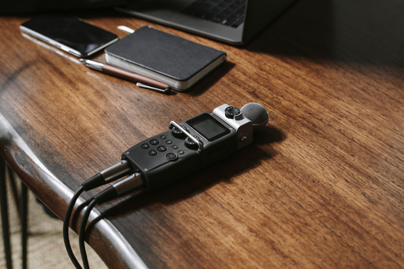 evp recorder on wooden desk next to black notebook and brown pen